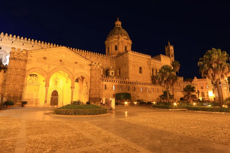 A stunning night view of the Palermo Cathedral, showcasing its detailed architecture under warm artificial illumination against a dark sky.
