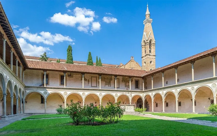 This image features excellent composition, capturing a wide view of a historic monastery courtyard with a prominent bell tower. The lighting is natural and even, highlighting the architectural details and the vibrant colors of the sky, grass, and stone. The image is sharp throughout, with all key elements in focus, contributing to its strong photo-realistic quality. Colors are accurate and appear natural. Overall, it's a very high-quality editorial image.