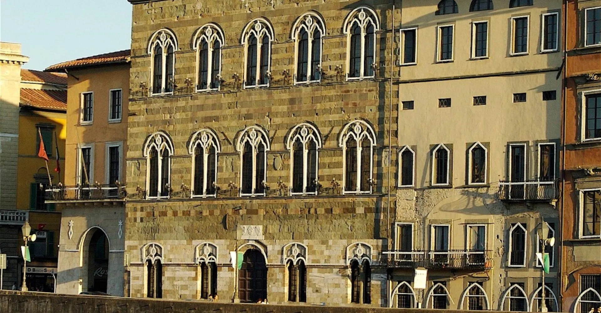 An editorial-style image showcasing the ornate windows and stone facade of a historic building. The image is sharp and well-lit, highlighting the intricate details of the gothic-style windows and the texture of the stone. Colors appear accurate and the image is highly photo-realistic.