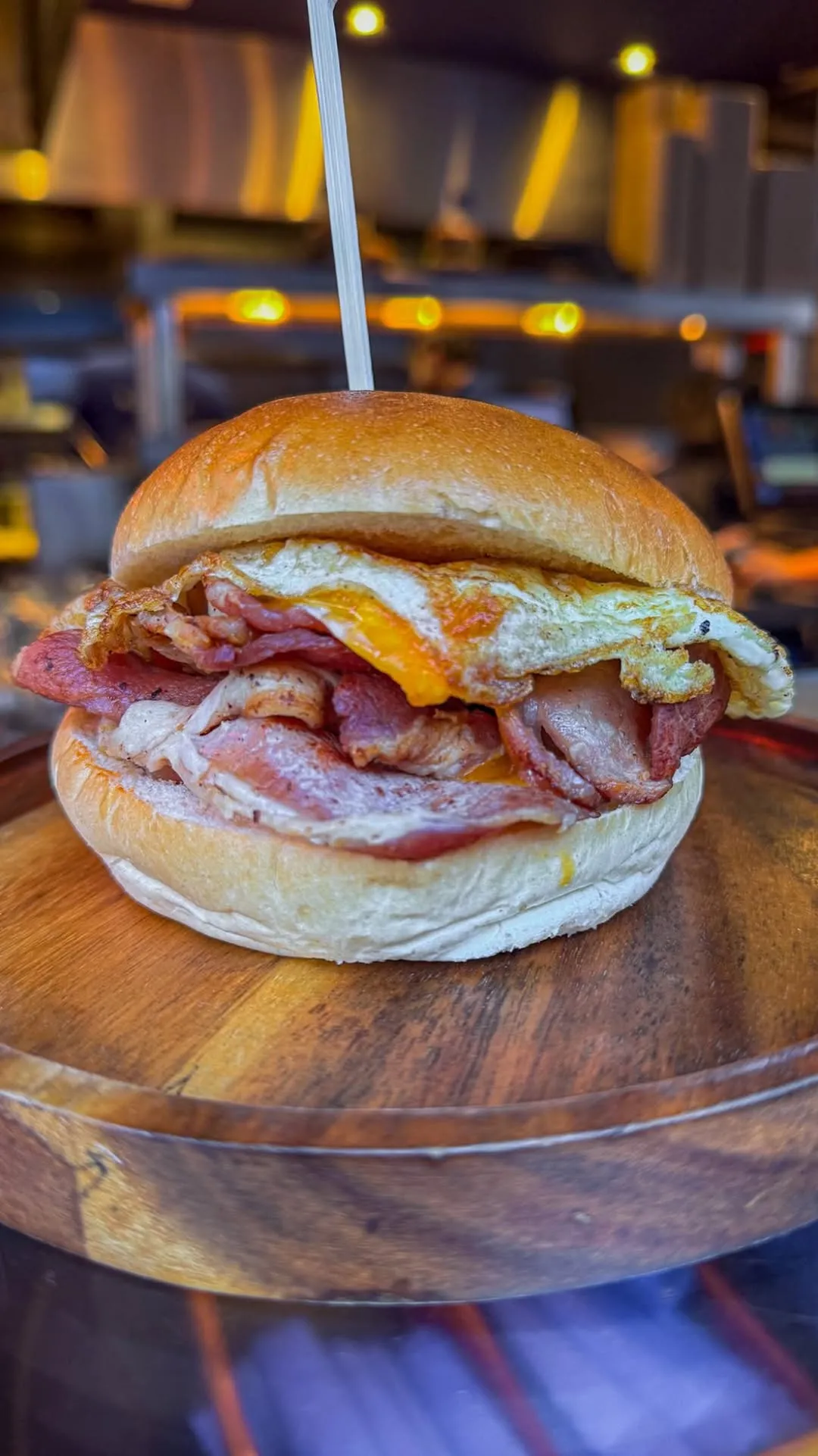 A close-up shot of a delicious breakfast sandwich featuring crispy bacon and a fried egg on a toasted bun, served on a rustic wooden board.