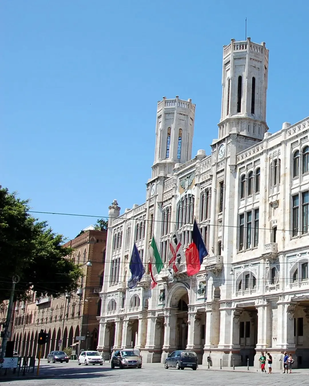 A well-lit and sharp photograph of a grand, classical building featuring two prominent towers and flags, set against a clear blue sky, showcasing detailed architectural elements.