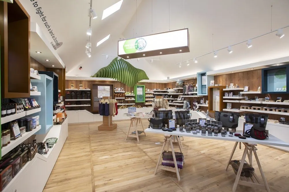 An interior view of a well-lit and organized retail store, showcasing merchandise on display shelves and tables, with a distinctive green wave-like sculpture on the ceiling.