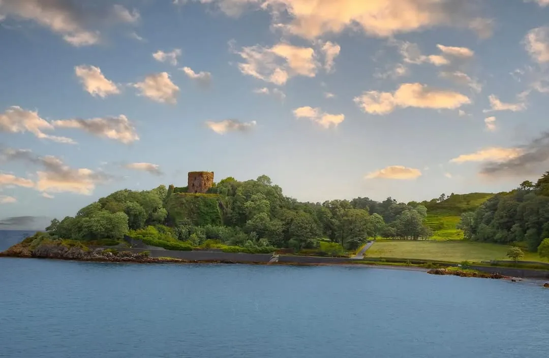 A well-composed and photo-realistic image featuring a historic castle on a lush, green hill, overlooking a serene body of water. The natural lighting is even, illuminating the scene well, and the colors are vibrant and accurate. The image is sharp throughout, with all key elements, including the castle, trees, and water, clearly in focus.