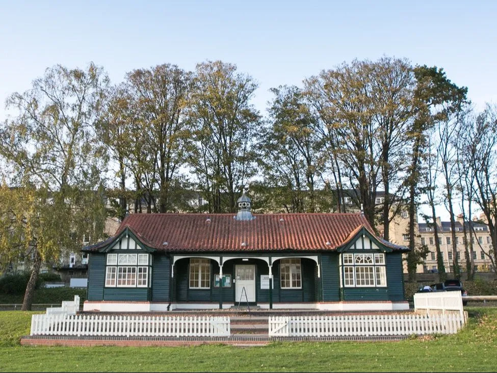 The image features a charming, well-maintained building with a dark green facade and a red tiled roof, framed by a white picket fence. The natural lighting is excellent, providing clear visibility of the building's details and accurate color representation. The composition is strong, with the building centrally placed, and the primary elements are sharp and in focus.