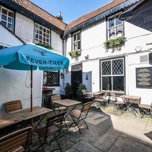 This image is a well-composed shot of a restaurant patio. It showcases a well-lit and inviting outdoor seating area with tables, chairs, and an umbrella. The composition is balanced, with the umbrella serving as a focal point. The lighting is excellent, creating a bright and airy atmosphere. The image is sharp, with good detail in the brickwork and the furniture. The colors are accurate and natural. The key elements are in focus, including the tables, chairs, and the umbrella. The image is photo-realistic and captures the essence of the space. The only minor weakness is the presence of a sign on the building, which could be considered an unwanted element. However, it's a small detail that doesn't detract significantly from the overall quality of the image. Overall, this image is a strong example of professional food photography, capturing the ambiance and appeal of the restaurant's outdoor seating area.