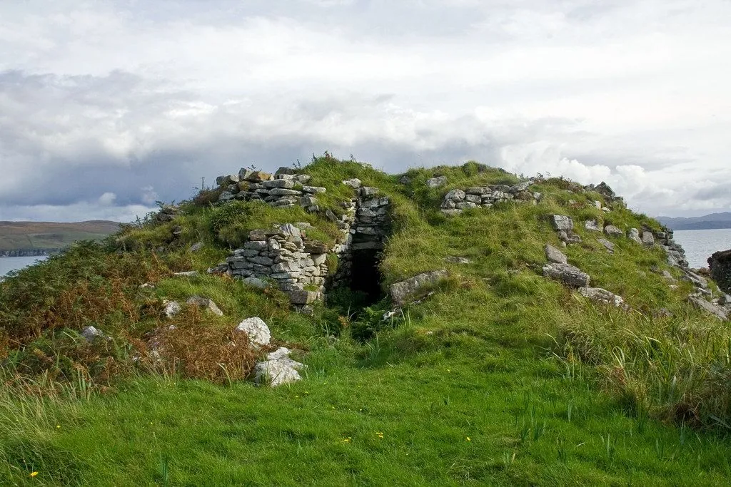 The image displays an ancient stone structure, possibly a tomb or dwelling, integrated into a grassy mound under an overcast sky. The composition adequately frames the subject.