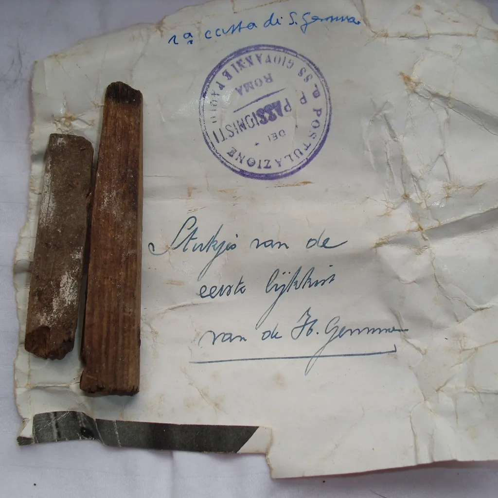 A flat lay photograph displaying two pieces of aged wood next to a crumpled, old document featuring handwritten text in ink and a prominent blue stamp. The items appear to be historical artifacts or relics.