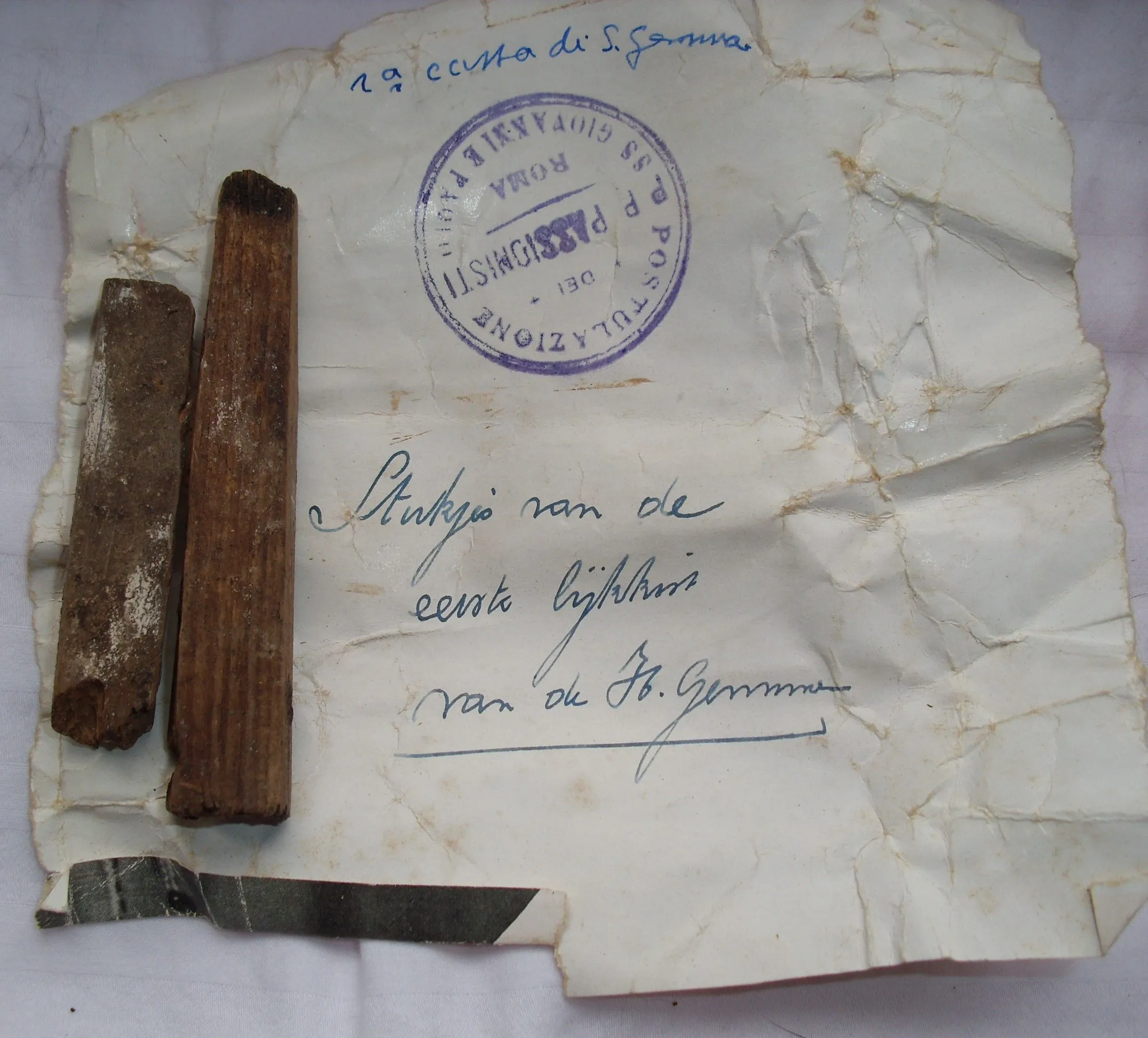 A flat lay photograph displaying two pieces of aged wood next to a crumpled, old document featuring handwritten text in ink and a prominent blue stamp. The items appear to be historical artifacts or relics.