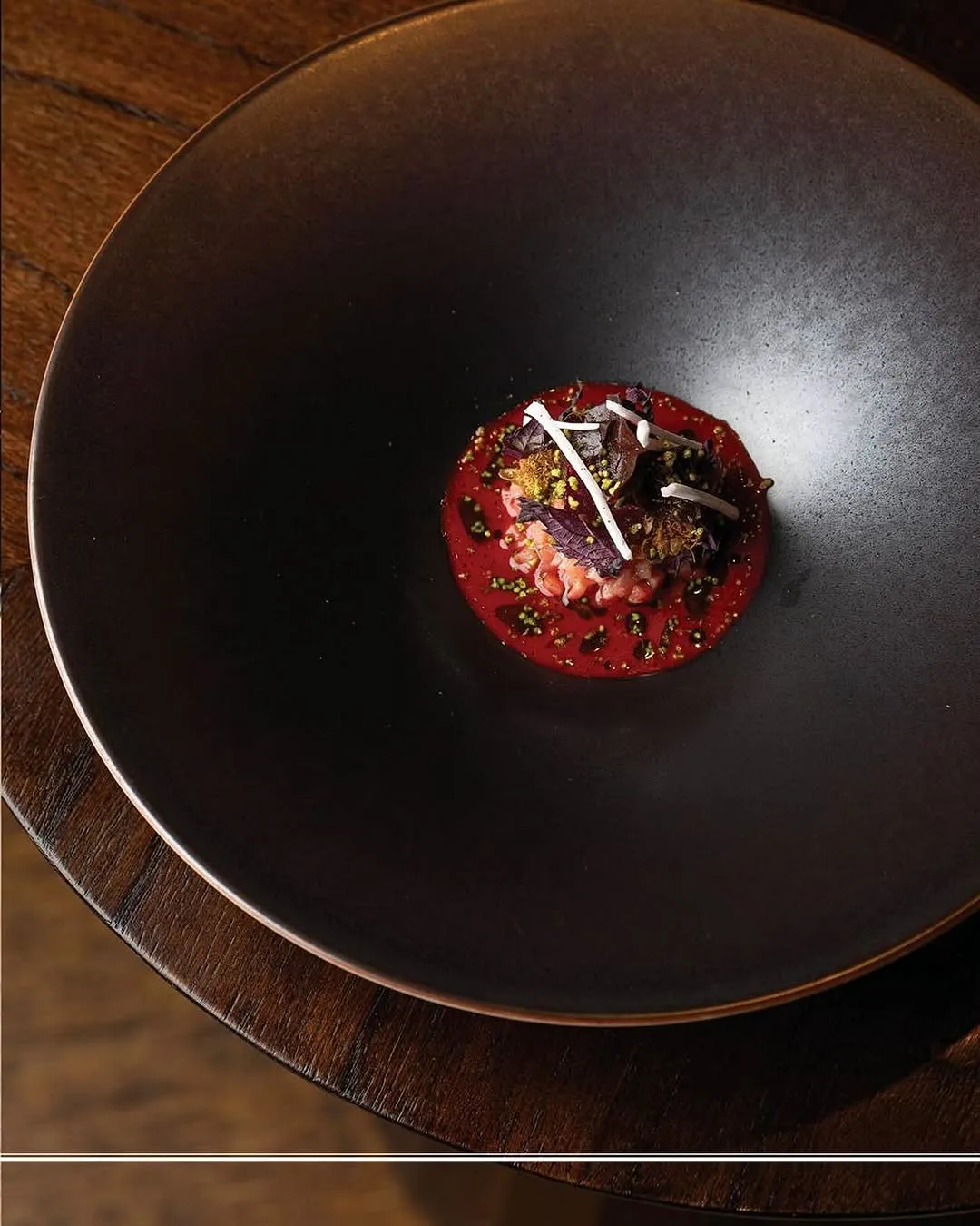 A gourmet dish presented on a dark, elegant plate, featuring a vibrant red base with intricate toppings. The composition is strong, placing the food centrally with some table surface providing context. The lighting is well-managed, enhancing the texture and color of the dish without harsh shadows. All key elements of the food are sharp and in focus, contributing to a photo-realistic and appealing image. The colors are rich and appear accurate.