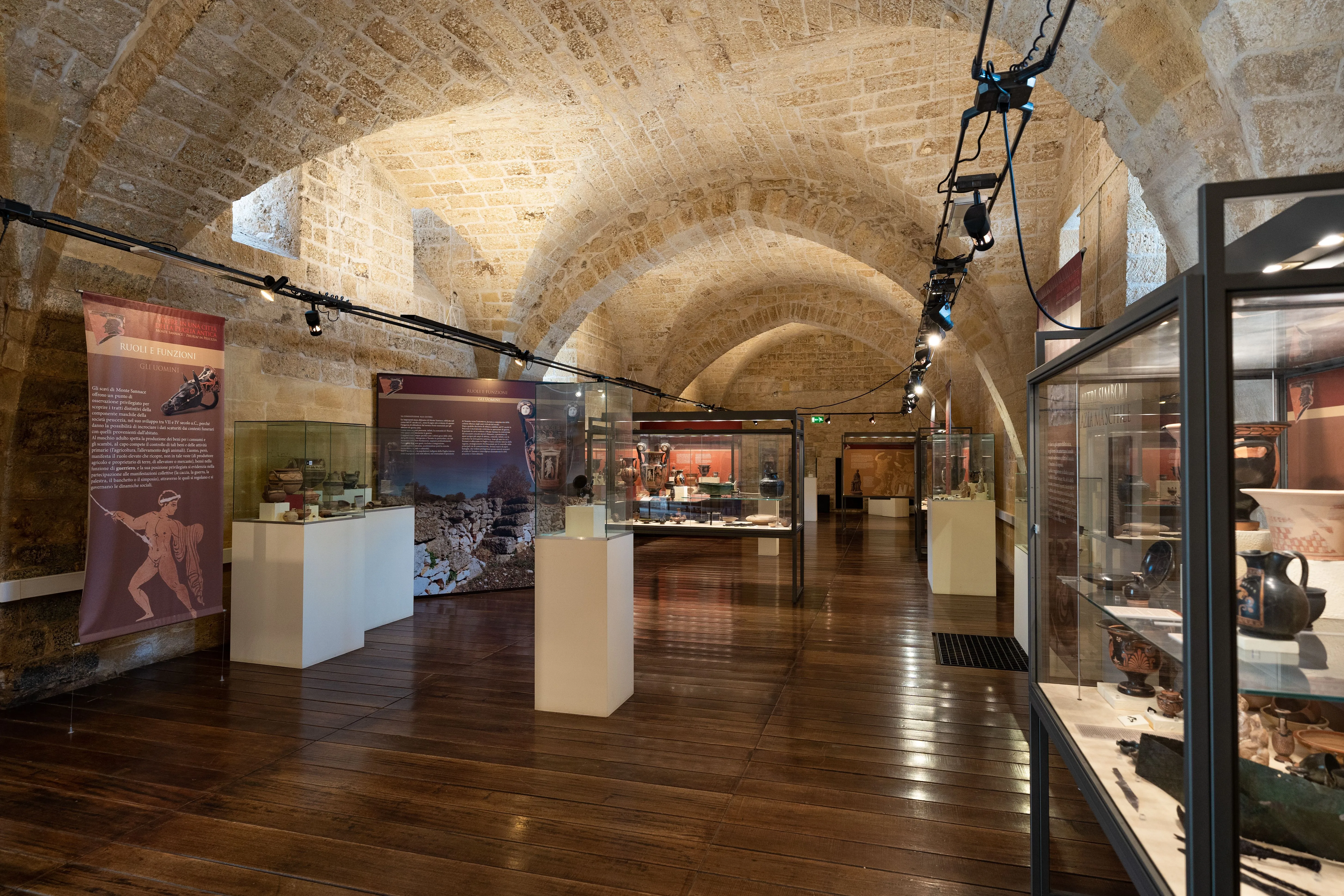 An editorial image of a well-preserved historical museum interior, showcasing its vaulted stone ceilings, wooden floors, and numerous display cases filled with artifacts and informational exhibits, illuminated by warm artificial lighting.