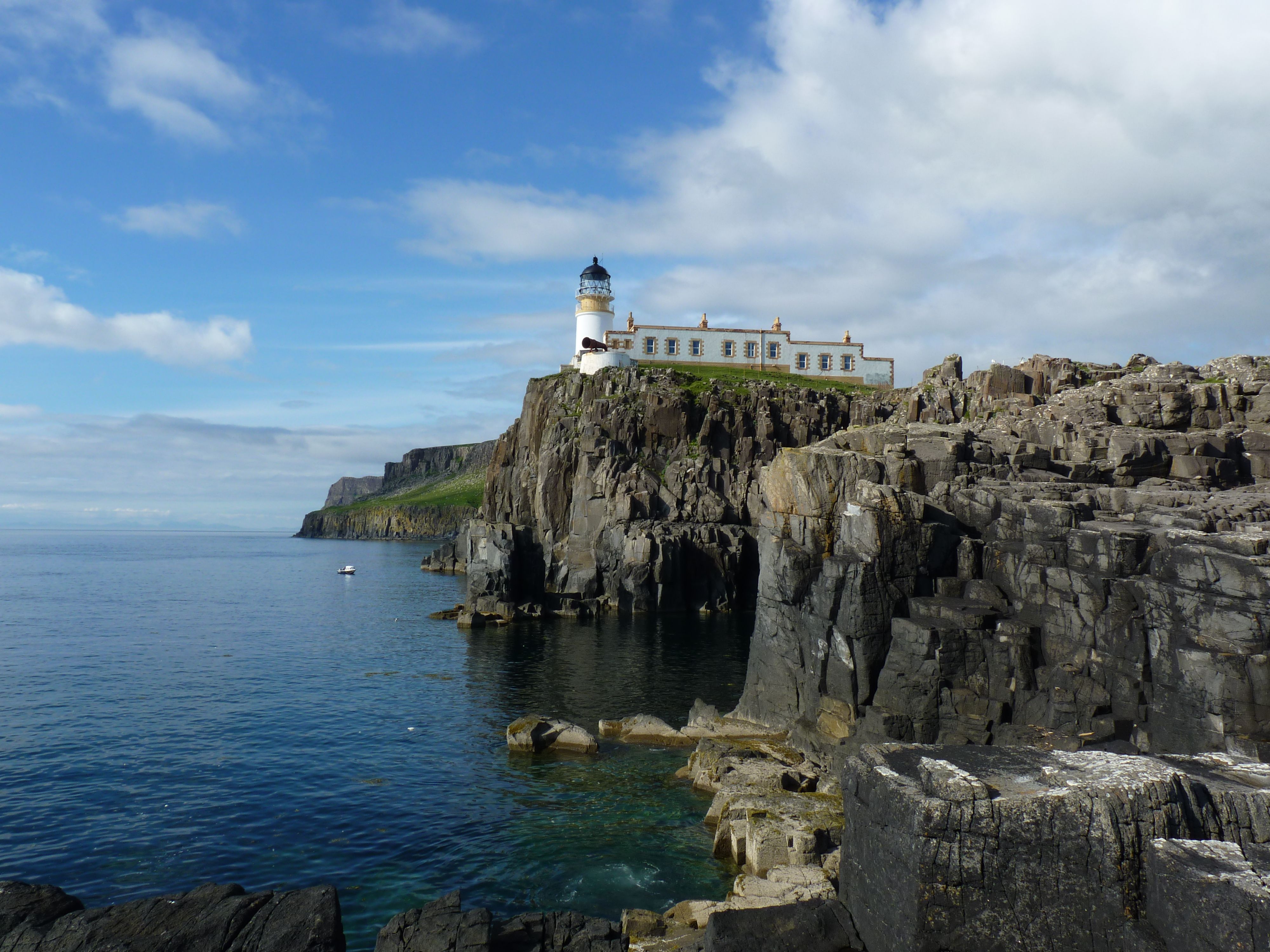 This image is an excellent example of exterior landscape photography, showcasing a lighthouse perched atop a dramatic cliff overlooking the sea. The composition is very strong, utilizing leading lines from the foreground rocks towards the lighthouse, which is positioned effectively within the frame. The lighting is superb, with clear, natural sunlight illuminating the scene, providing good contrast and depth without harsh shadows. The image is exceptionally sharp across the entire depth of field, with both the foreground elements and the distant lighthouse in crisp focus. Colors are vibrant and accurate, reflecting the natural beauty of the scene, and the overall realism is outstanding. All key elements, particularly the lighthouse and the rugged cliffs, are in sharp focus.