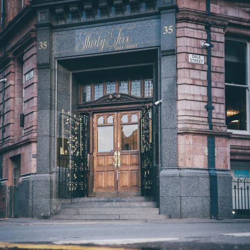 The image is well-composed, capturing the building's entrance with a balanced perspective. The lighting is adequate, providing good visibility of the details. The image is sharp, showcasing the intricate details of the architecture. The colors are accurate and natural. The image is photo-realistic, accurately representing the building's exterior. The key elements, including the entrance, sign, and surrounding architecture, are in focus. However, the presence of text on the sign and the street name plaque makes it an unwanted element. Therefore, the image score is 0.