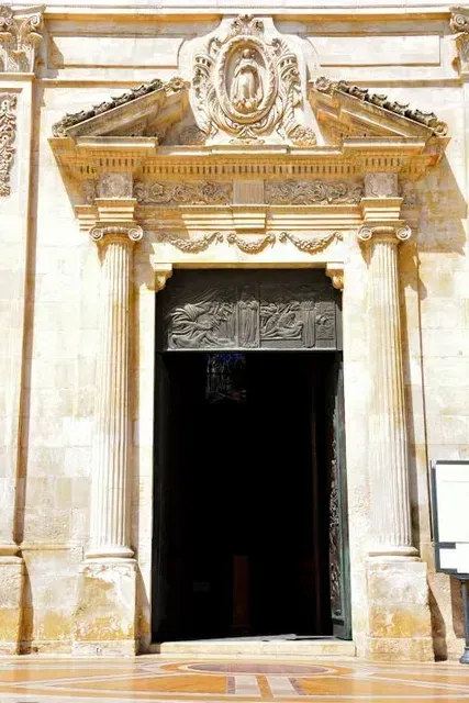 A detailed, close-up view of an ornate stone entrance to a historic building, featuring decorative columns, intricate carvings, and a dark arched doorway.