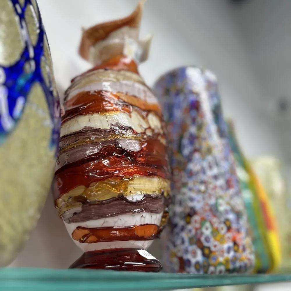 The image features a collection of decorative glass vases displayed on a shelf, with a horizontally striped vase in the foreground as the primary subject. The use of shallow depth of field effectively isolates the main vase, blurring the background elements. The colors are vibrant and appear natural.