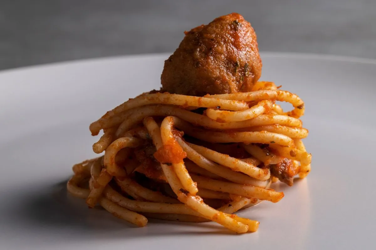 A close-up shot of spaghetti with a meatball on a white plate.
