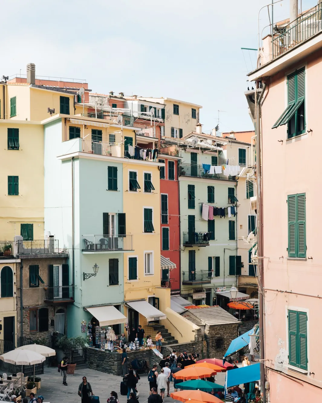 An image showcasing a vibrant array of colorful buildings with traditional green shutters, set against a bright sky, characteristic of a coastal European village. Laundry is visible hanging from balconies, adding to the lived-in atmosphere.