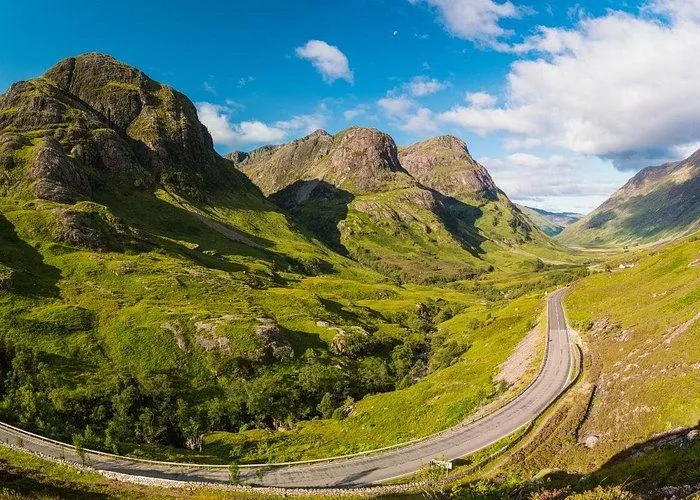 An exceptionally well-composed and vibrant photograph showcasing a winding road through a lush green mountain valley under a bright blue sky.