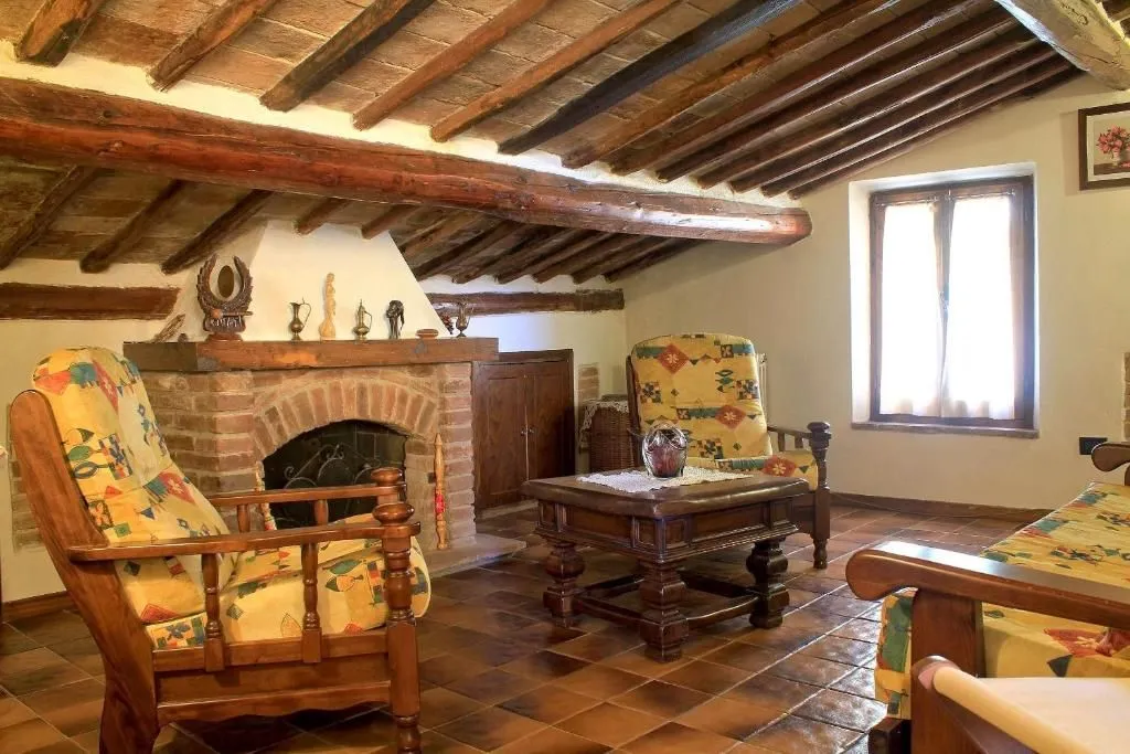 An editorial style image showcasing a traditional living room with a brick fireplace, wooden beamed ceiling, and terracotta floor tiles.