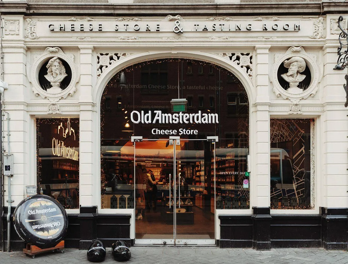A well-composed, sharp, and photo-realistic image of the "Old Amsterdam Cheese Store" facade. The architectural details are captured with good focus and natural lighting. Colors are accurate, and the entire storefront, including the signage, is clearly visible and in focus.