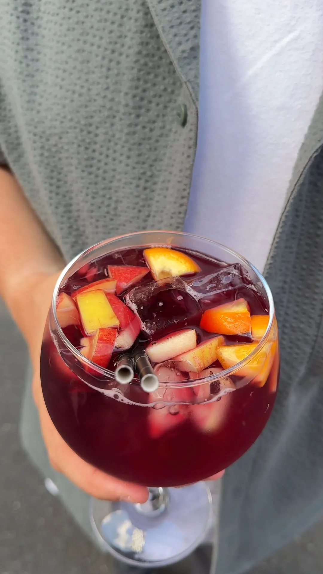 A vibrant and well-composed close-up of a sangria glass, featuring visible fruit pieces (apples and oranges) and ice. The lighting is natural, highlighting the drink's rich color and the freshness of the fruit. The image is sharp, and the background is softly blurred, keeping the focus entirely on the beverage.