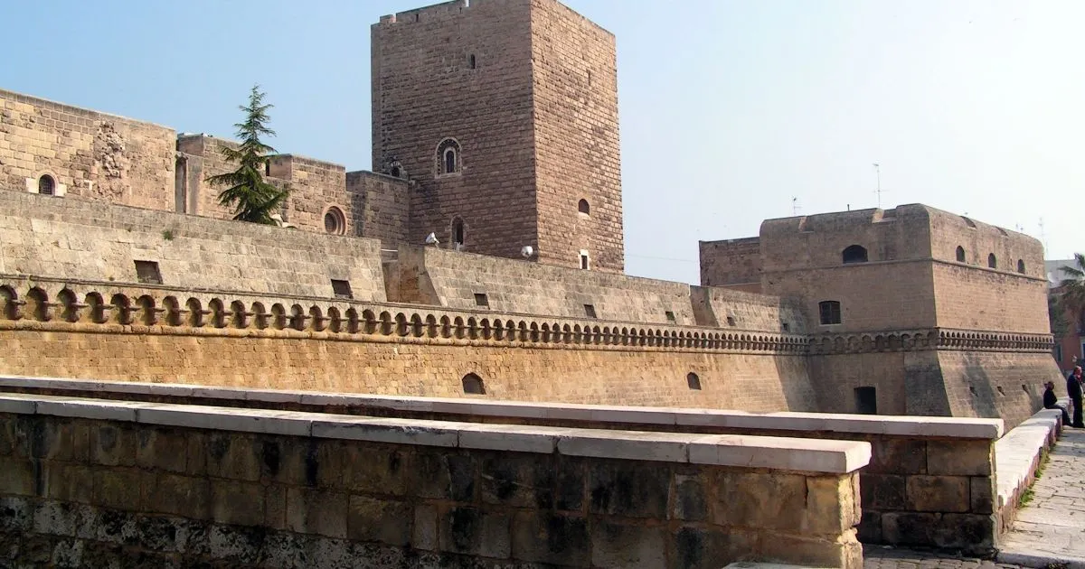 The image features a stone castle or fortress, captured in an editorial style. The main architectural elements, including the towering structure and the intricate detailing of the walls, are sharply in focus. The lighting is good, illuminating the stone work and showing accurate colors typical of ancient masonry. The photo-realistic quality is high, presenting a clear and natural view of the historical site.