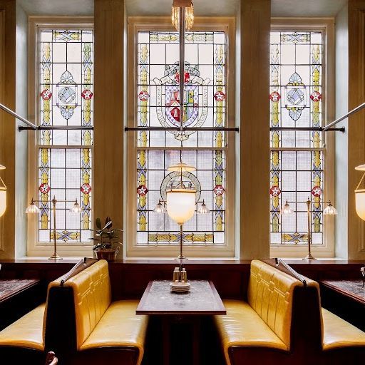 This image is an example of interior photography. It shows a restaurant interior with stained glass windows, booth seating, and a chandelier. The composition is well-balanced and uses leading lines to draw the eye to the stained glass windows, which are the main focus of the image. The image is well-lit and appears to be taken during the day with natural light. It seems to be color-accurate with no apparent color cast or saturation issues. The sharpness is excellent, and even the finer details are clearly visible. Based on the above criteria: - The image successfully captures the beauty of the space, with a strong focus on the key elements. - There are no unwanted elements in the image. Score: 95 Strengths: - Excellent composition and use of leading lines - Well-lit and color-accurate - Very sharp with excellent detail capture Weaknesses: - None