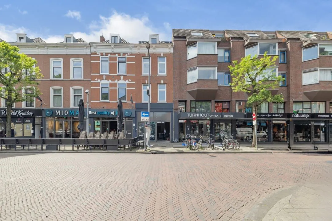 This image effectively captures a vibrant street scene with a row of commercial buildings under natural daylight. It is sharp, well-lit, and photo-realistic with accurate colors and good focus on the main subjects. While generally well-composed, the perspective is slightly tilted, and the foreground occupies a substantial portion of the frame. The presence of bikes and stacked patio furniture adds realism but also a minor element of clutter.
