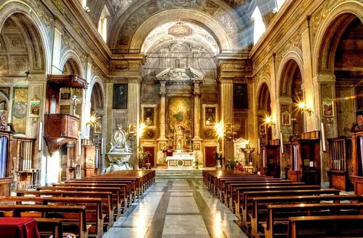 An interior view of a grand church or cathedral, showcasing ornate details, rows of wooden pews leading towards a brightly lit altar, and dramatic rays of light streaming through upper windows.