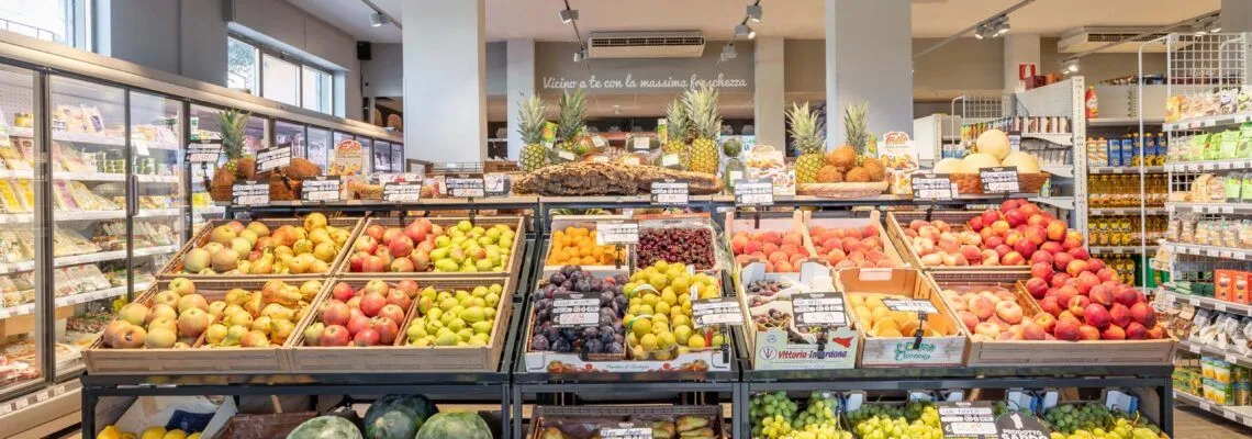An inviting view of a fresh produce section in a grocery store, featuring a vibrant assortment of fruits like pineapples, apples, plums, cherries, and citrus arranged neatly in wooden crates.