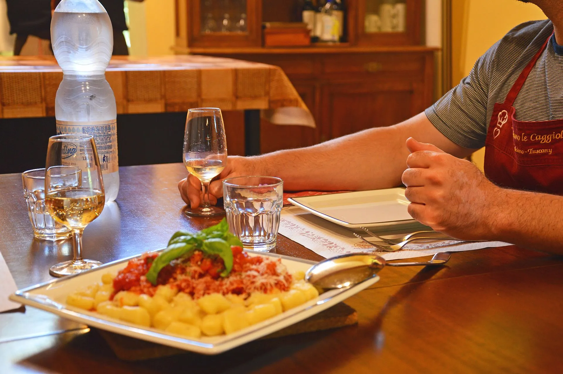 The image is well-composed with the food as the clear focal point, supported by good depth of field. The lighting is soft and natural, enhancing the food's appearance. Key elements, especially the gnocchi and basil, are sharp and in focus. Colors are accurate and appealing, contributing to the photo-realistic quality. The background, though blurred, is a bit busy, which slightly detracts from a perfectly clean aesthetic.