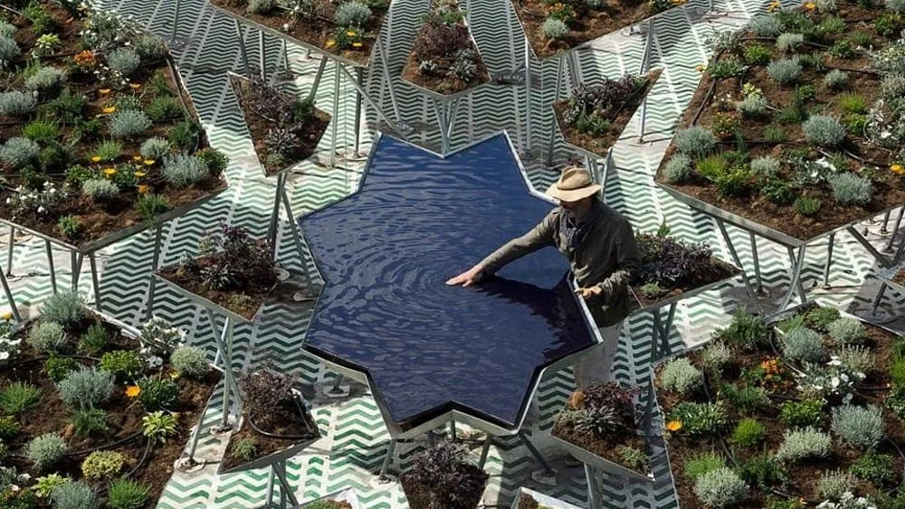 An aerial shot capturing a man interacting with a star-shaped water feature, surrounded by numerous triangular plant beds, creating a unique geometric garden design.