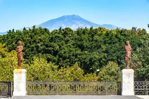 The image features a well-composed landscape with a prominent mountain in the background, lush green trees in the middle ground, and an ornate fence in the foreground. The lighting is good, contributing to natural and vibrant colors. The image is sharp, and key elements are in focus, making it appear photo-realistic. While the composition is good, it isn't exceptionally dynamic.
