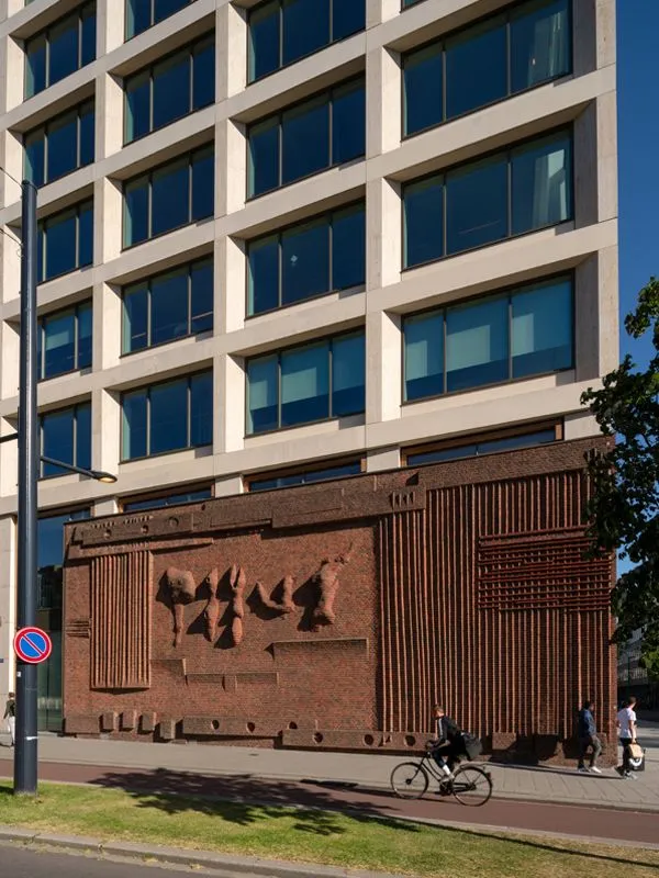 The image features a well-composed shot of a building facade, showcasing a detailed brick relief at its base and a modern structure above. The lighting is excellent, highlighting the textures and forms, and the image is sharp with accurate colors, contributing to its photo-realistic quality. All key architectural elements are in clear focus.