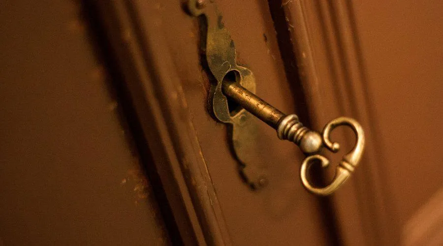 A close-up, editorial-style image of an old key inserted into a keyhole on a wooden surface.