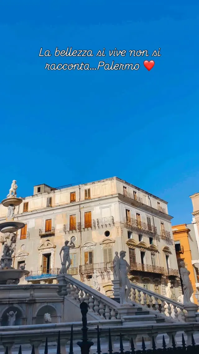 An outdoor shot featuring a historical building with statues and part of a fountain in the foreground, set against a bright blue sky.