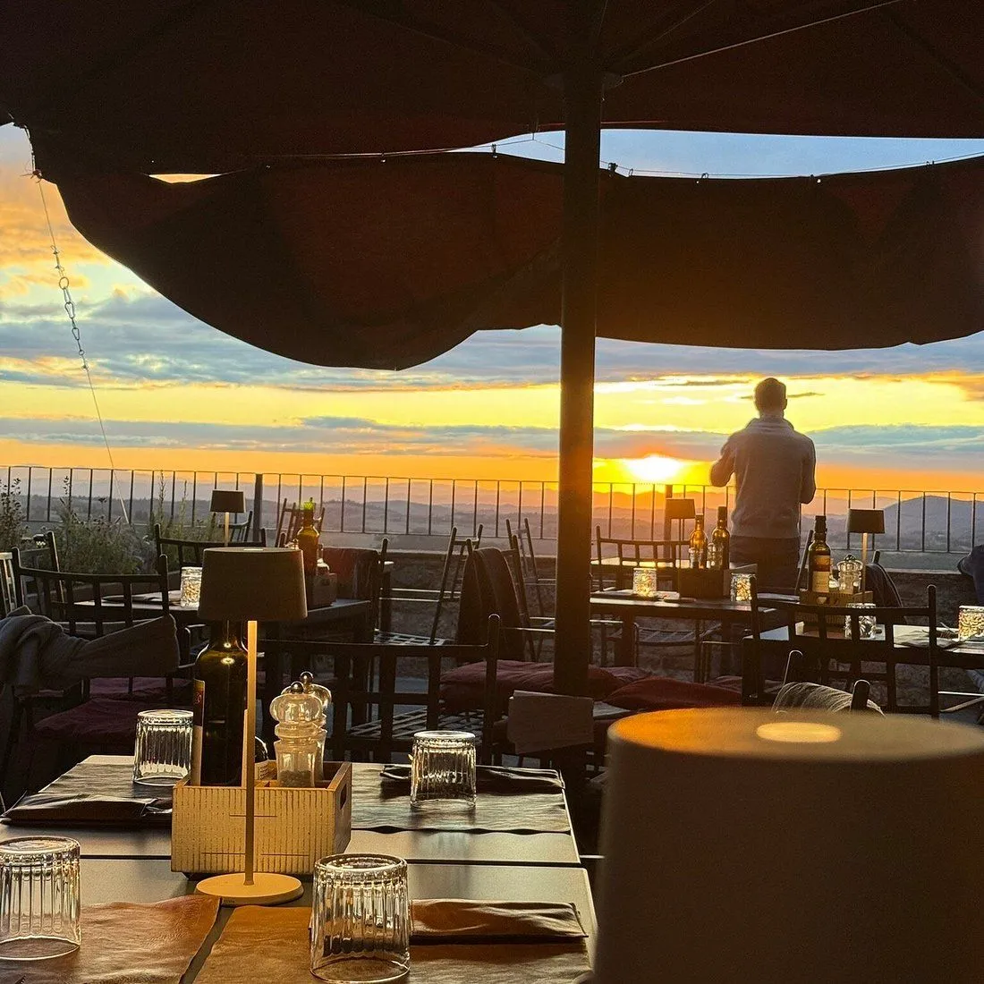 An editorial image of a restaurant terrace at sunset, showcasing a person observing the scenic view and the warm ambiance of the setting.