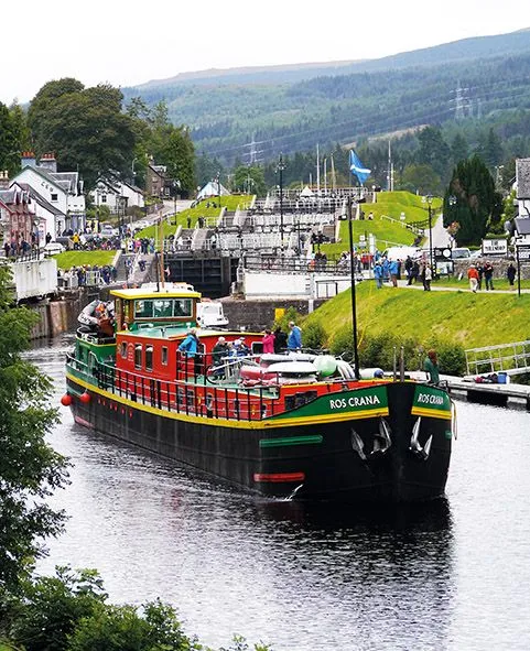 The image features a colorful canal boat navigating a lock system, surrounded by lush green hills and quaint buildings. The composition effectively captures the scene, with natural, even lighting. Colors are vibrant and accurate, contributing to the photo-realistic quality. Key elements, including the boat and the background lock system, are acceptably in focus, though the overall sharpness could be improved.