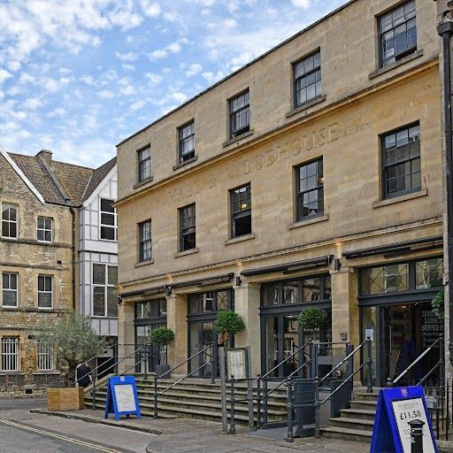 This image is a well-composed exterior shot of a restaurant. The building is the main subject and is well-lit, showcasing its stone facade and architectural details. The image is sharp, with good detail in the windows, doors, and signage. The colors are accurate and the image is photorealistic. The key elements, such as the building and its entrance, are in focus. The image contains some unwanted elements, such as the streetlamp and the tree, but they are not overly distracting and do not detract significantly from the overall quality of the image. The image is visually appealing and effectively conveys the character of the restaurant. The score is 85, with deductions for the unwanted elements and the presence of text on the signboard.