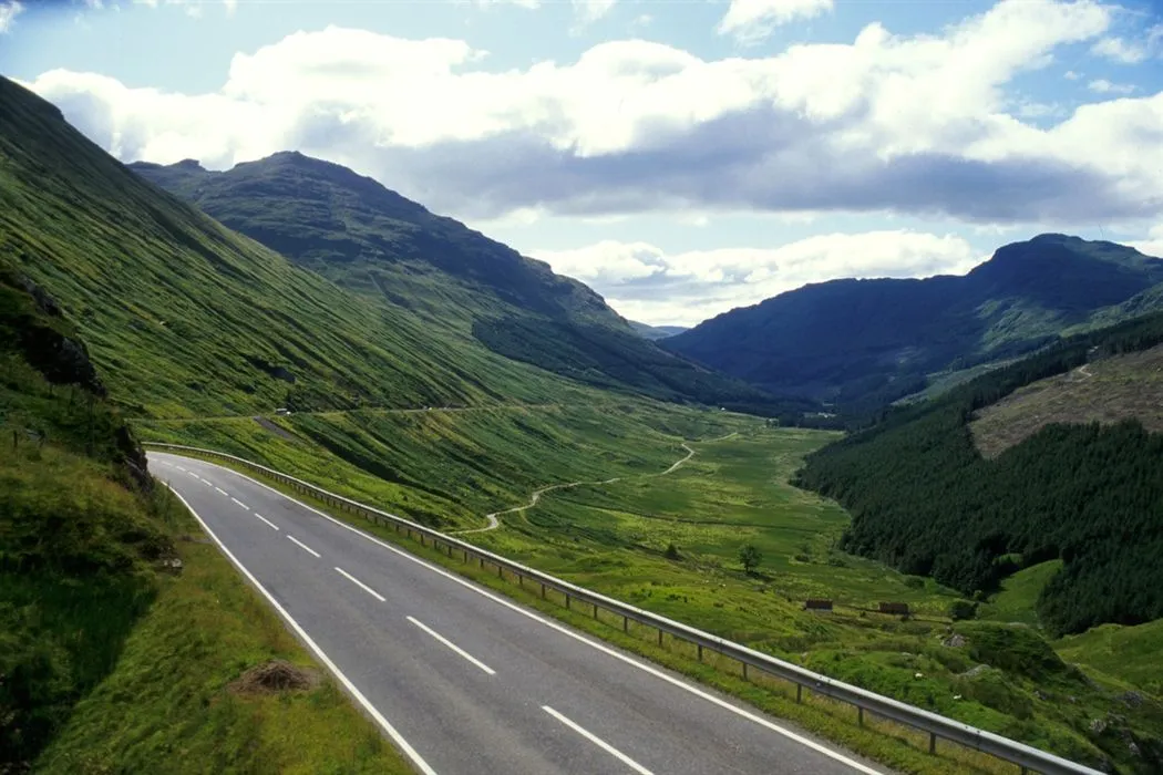 A beautiful and well-composed landscape photograph featuring a winding road through lush green mountains and a valley under a partially cloudy sky. The image exhibits good sharpness and color accuracy, contributing to its strong photo-realistic quality.
