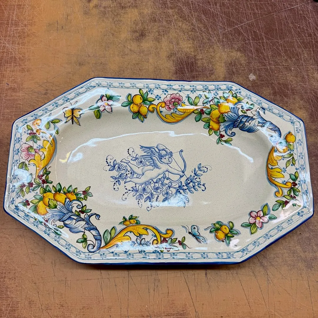 The image displays a decorative ceramic platter with a detailed hand-painted design. The composition is good, centering the platter effectively. The lighting is even, and the image is sharp with accurate colors, highlighting the intricate patterns and motifs clearly. All key elements of the platter are in sharp focus. The main detractor is the background, a scratched wooden surface, which although not an unwanted element, does not enhance the presentation and slightly lowers the composition score.