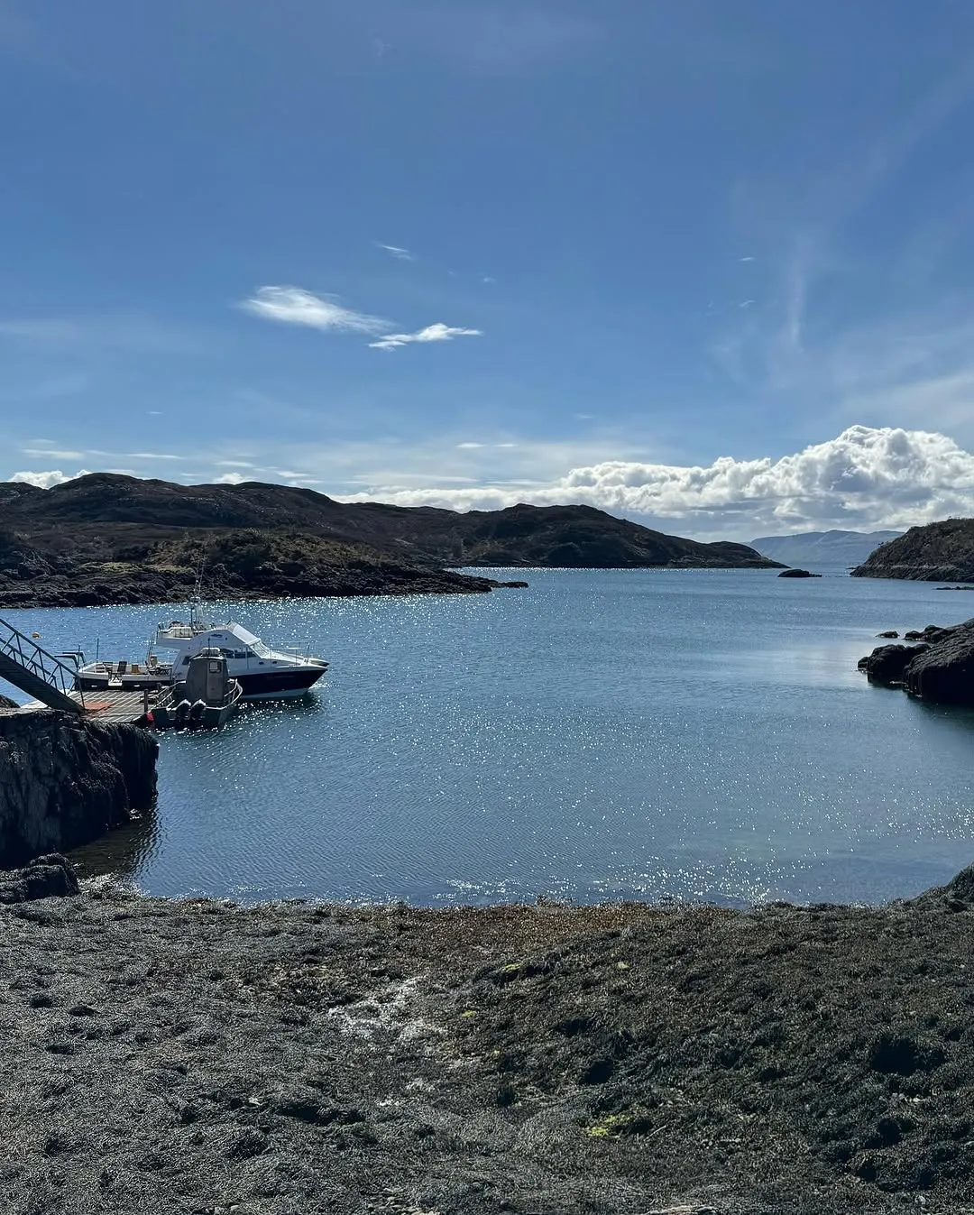 A vibrant image of a boat docked in a calm bay, surrounded by rugged coastal hills under a clear blue sky.