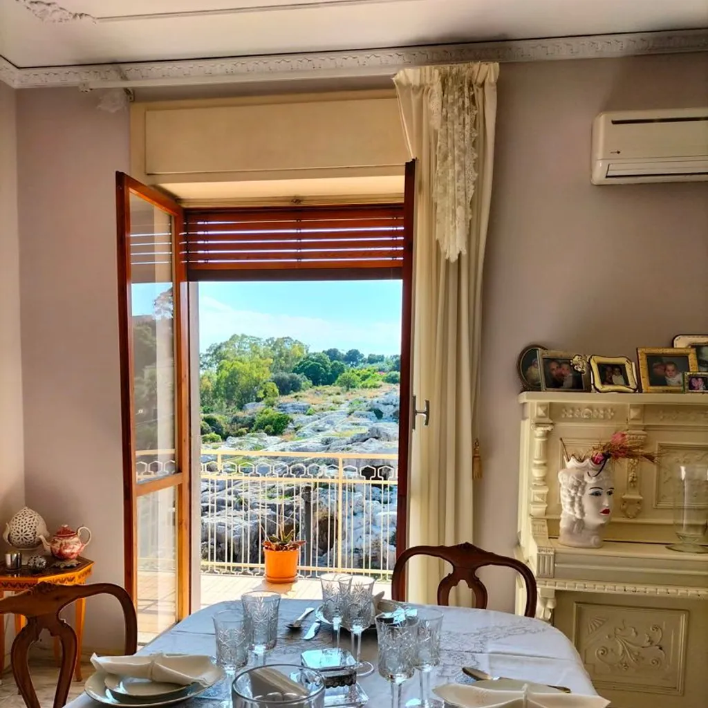 The image is a well-composed editorial-style shot of a dining room with a scenic balcony view. Its strengths include its photo-realistic quality, sharp focus on the main elements like the set table and the landscape, and effective framing that provides depth. However, the lighting presents a challenge due to the high contrast between the bright exterior and the dimmer interior, leading to some underexposure inside and minor overexposure in the sky. The composition could be marginally improved with more balanced framing and careful attention to elements at the edges.