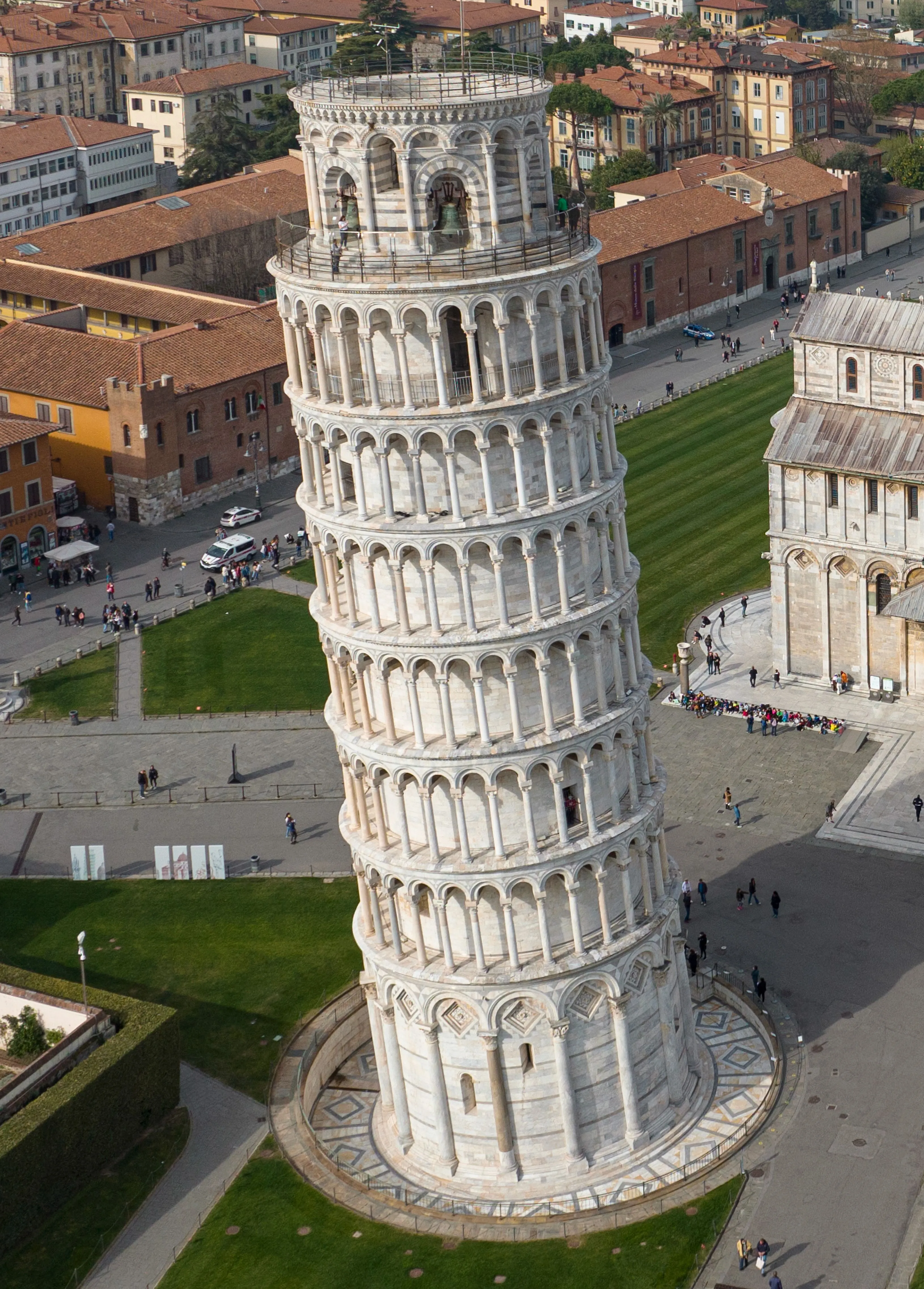 An aerial-like view of the Leaning Tower of Pisa under bright daylight, showing its distinctive lean and surrounding piazza.