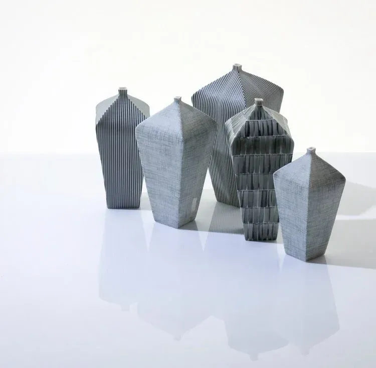 A high-quality image showcasing five distinct sculptural vases against a clean white background. The composition is excellent, with a balanced arrangement of the objects and effective use of negative space. The lighting is soft, even, and professional, enhancing the forms and textures of the vases. All key elements are in sharp focus, and the image exhibits strong photo-realism and accurate color representation.
