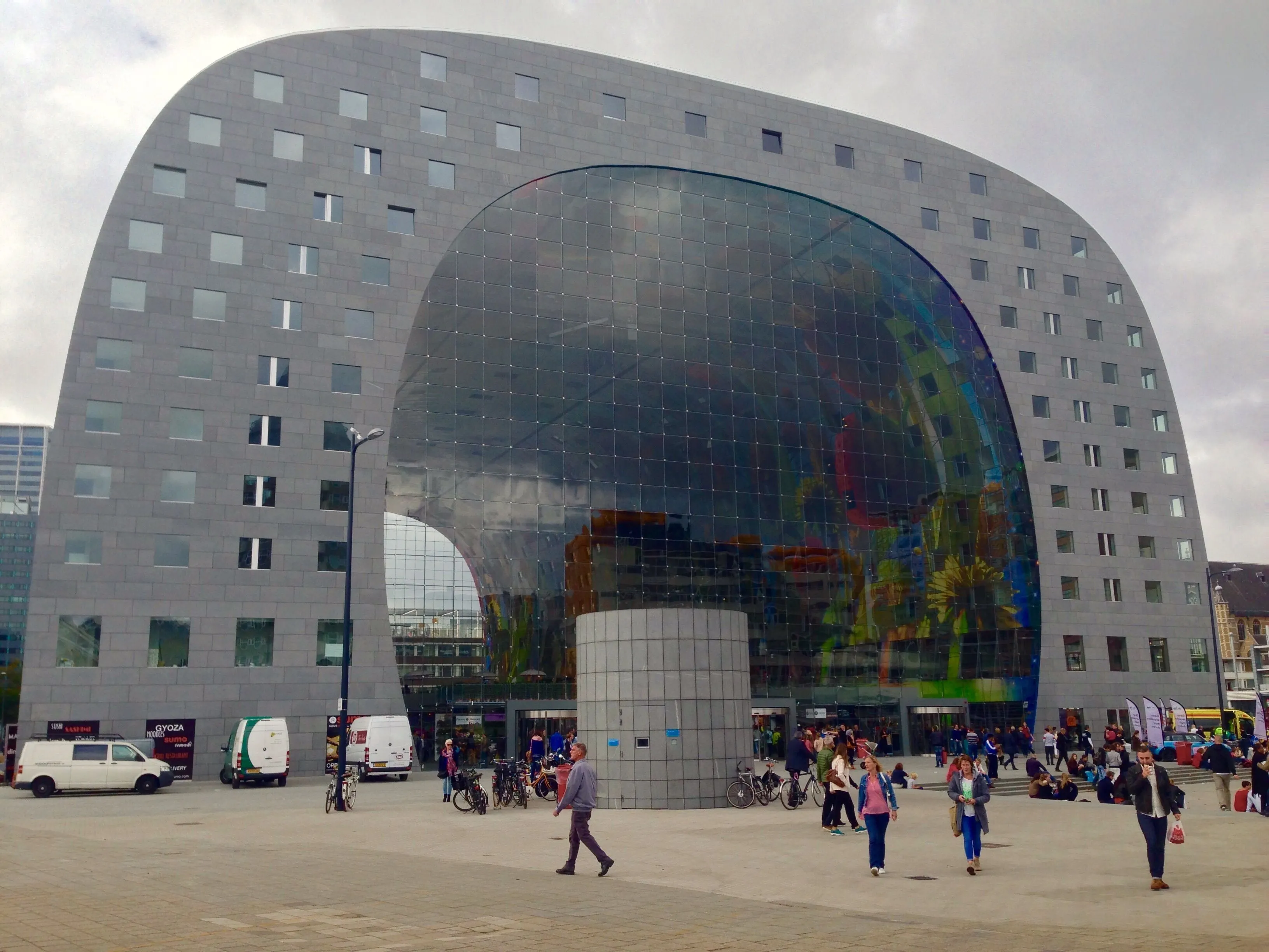 An editorial image showcasing the unique, modern architecture of a building with a large arched glass facade. The image is photo-realistic and captures the vibrant reflections within the glass structure. The natural, albeit overcast, lighting ensures accurate colors.