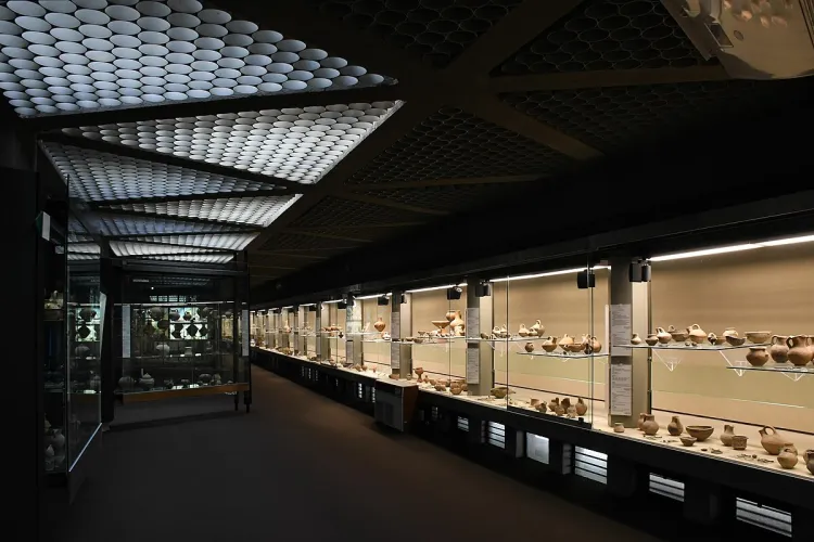 The image effectively captures a museum exhibit hall, showcasing numerous artifacts in display cases. The composition provides a good sense of the long hall, and the key elements, the artifacts, are well-lit and in focus. The image is sharp and photo-realistic. However, the overall lighting in the hall is uneven, with significant dark areas on the floor and ceiling outside of the display case illumination, which slightly detracts from the image's overall brightness and detail in those regions.