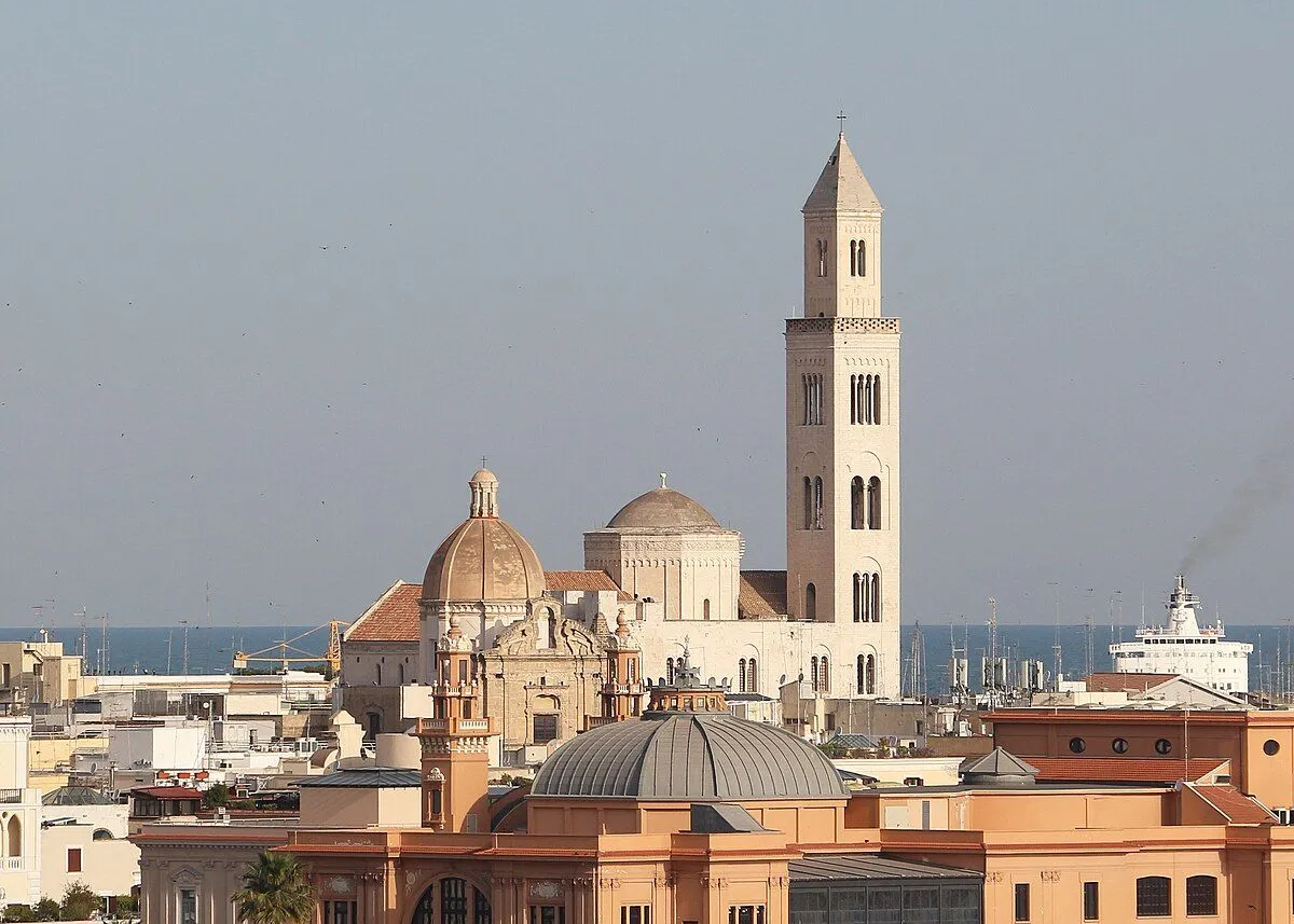An editorial-style image capturing an elevated view of a historic cathedral and surrounding urban landscape with the sea in the background.