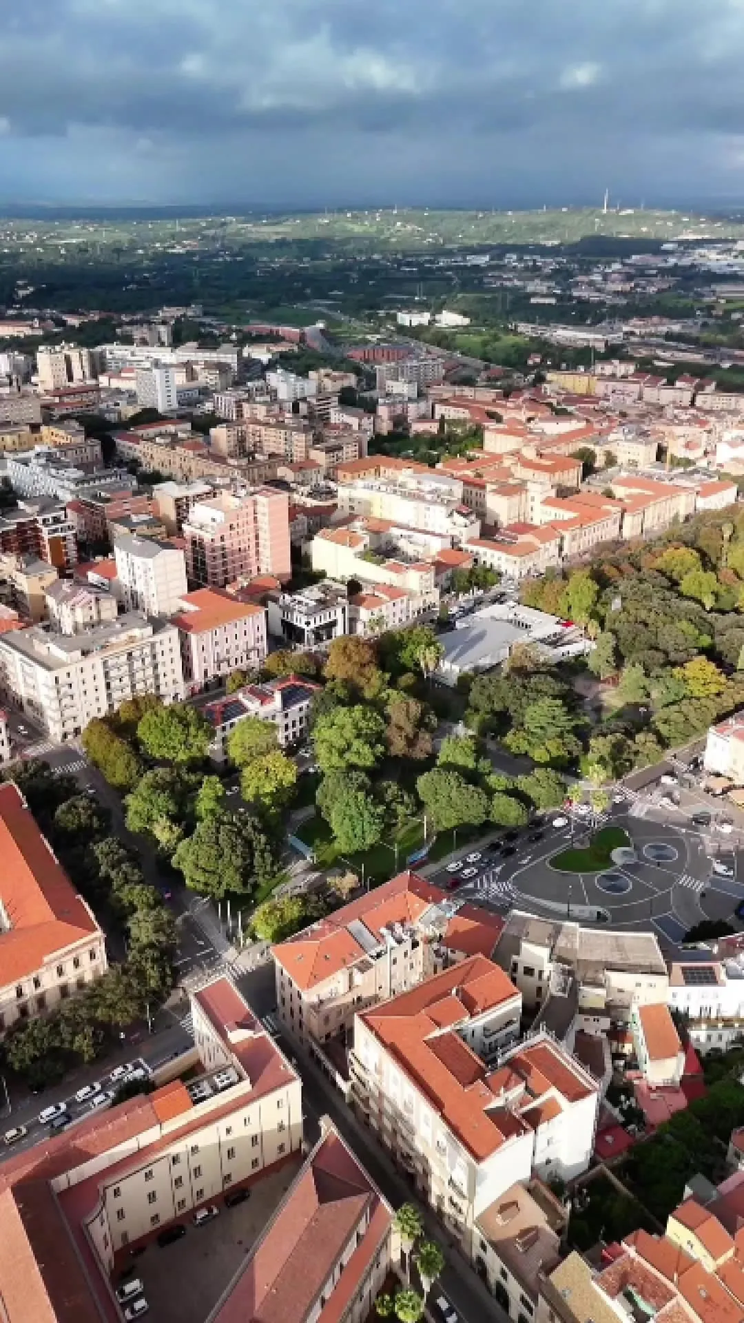 An aerial photograph capturing a dense urban area with a significant central park and surrounding buildings, along with roads and vehicles. The image is taken during daylight, showing clear skies and natural light.