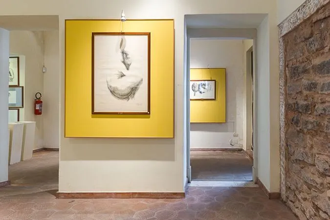 The image effectively captures an editorial view of an art gallery, featuring a prominently displayed artwork. It is highly photo-realistic, and the primary elements, especially the main artwork, are sharp and in focus. However, the composition is slightly hampered by the light fixture appearing at the top of the frame and marginally cutting off the artwork's frame. The lighting, while generally sufficient, presents some challenges with a visible hotspot on the main artwork and uneven illumination in certain areas, particularly the deeper parts of the hallway. Colors appear accurate and natural.