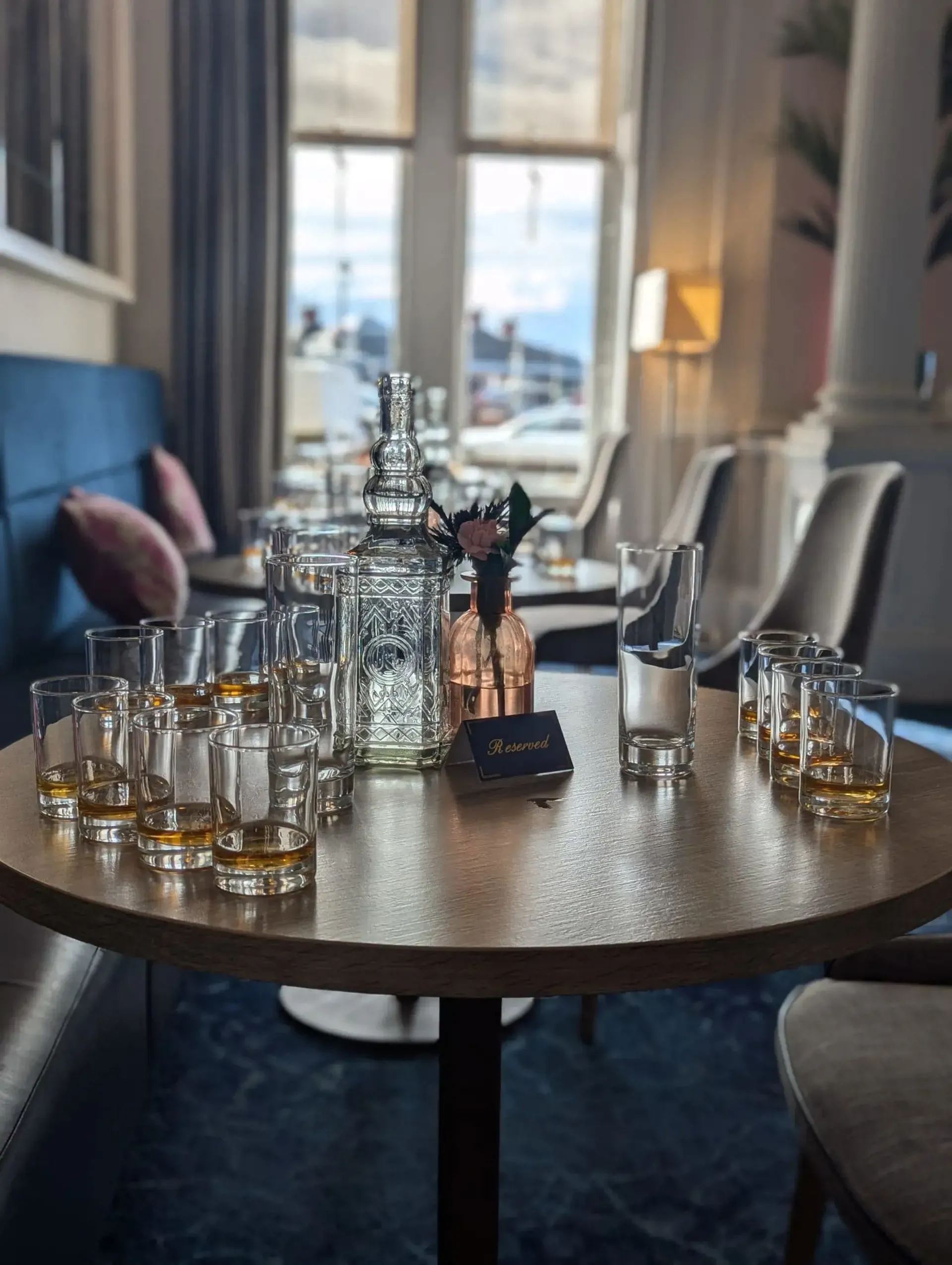 The image is well-composed, featuring a clear and well-arranged setup for what appears to be a whiskey tasting. The lighting is natural and generally good, creating a pleasant atmosphere. Key elements such as the glasses, decanter, and the "Reserved" sign are sharp and in focus, contributing to a strong sense of photo-realism. Colors are accurate, providing a true-to-life representation of the scene. The depth of field is effectively used to highlight the main subject while blurring the background.